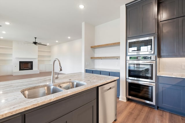 kitchen featuring light stone countertops, appliances with stainless steel finishes, sink, a brick fireplace, and ceiling fan