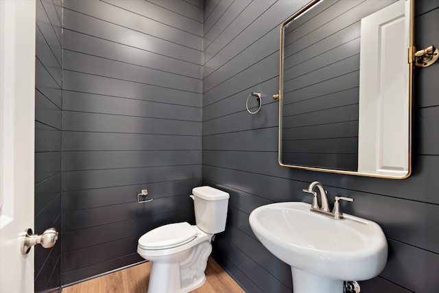 bathroom featuring wood walls, wood-type flooring, toilet, and sink