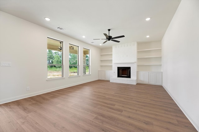 unfurnished living room featuring built in shelves, ceiling fan, hardwood / wood-style flooring, and a fireplace