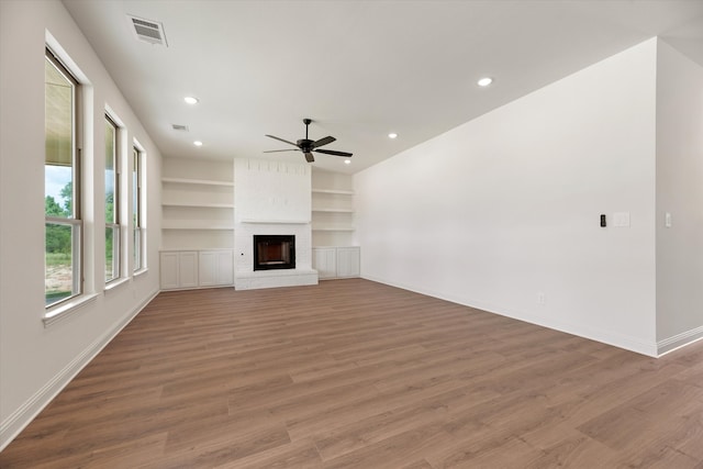 unfurnished living room featuring hardwood / wood-style floors, ceiling fan, a fireplace, and built in shelves