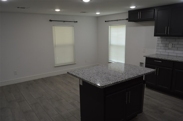 kitchen featuring dark hardwood / wood-style floors, light stone countertops, tasteful backsplash, and a kitchen island