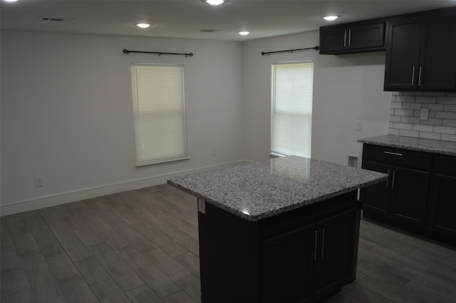 kitchen featuring a kitchen island, light stone counters, dark hardwood / wood-style floors, and backsplash