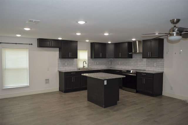 kitchen with ceiling fan, light stone counters, wall chimney exhaust hood, and stainless steel range with electric stovetop