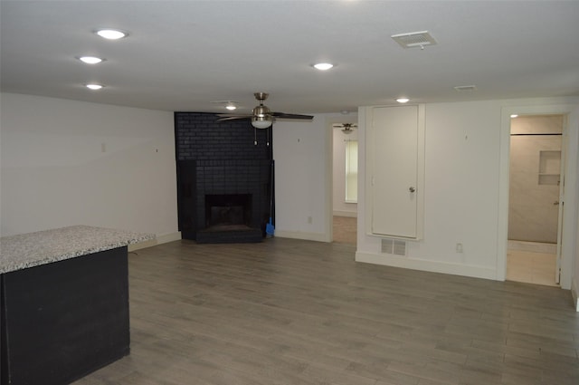 unfurnished living room featuring ceiling fan, a brick fireplace, and dark wood-type flooring