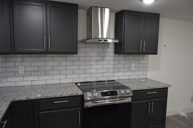 kitchen with stainless steel electric stove, wall chimney exhaust hood, light stone countertops, hardwood / wood-style floors, and decorative backsplash