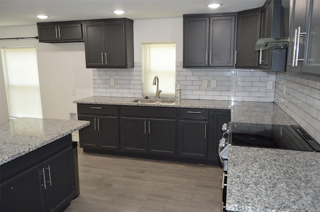 kitchen featuring stainless steel electric stove, sink, hardwood / wood-style flooring, light stone counters, and decorative backsplash