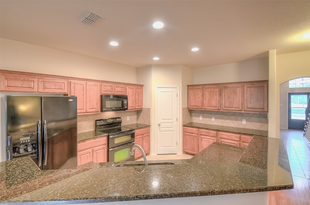 kitchen with black appliances, sink, backsplash, light tile patterned floors, and dark stone countertops