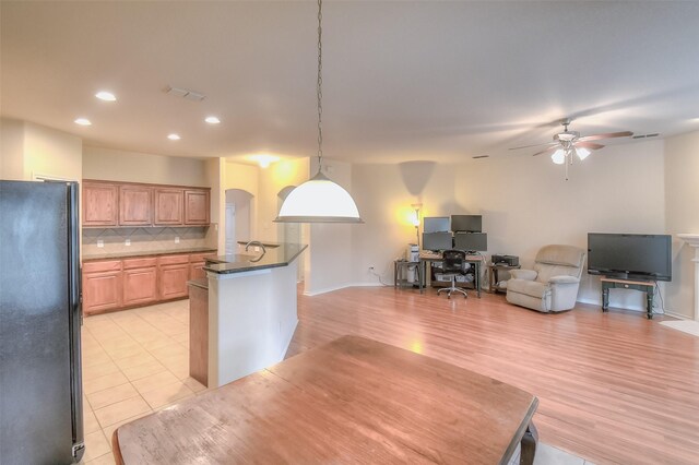 kitchen with hanging light fixtures, backsplash, light hardwood / wood-style floors, ceiling fan, and black fridge