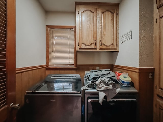 washroom with cabinets, washer and clothes dryer, and wooden walls