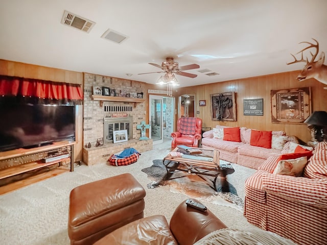 living room with a brick fireplace, carpet, wooden walls, and ceiling fan