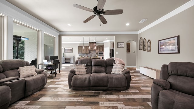 living room with dark wood-type flooring, ceiling fan, sink, and crown molding