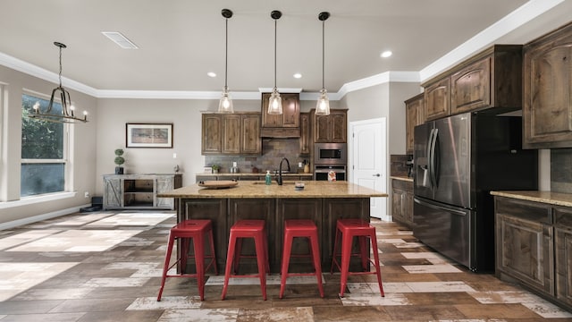 kitchen featuring appliances with stainless steel finishes, hanging light fixtures, decorative backsplash, a kitchen island with sink, and ornamental molding