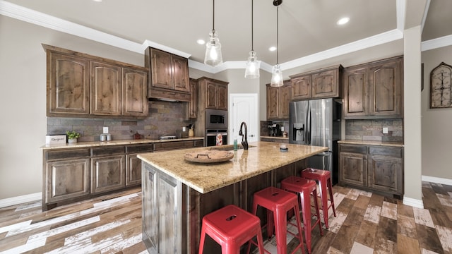 kitchen featuring appliances with stainless steel finishes, crown molding, decorative backsplash, a kitchen island with sink, and hardwood / wood-style flooring