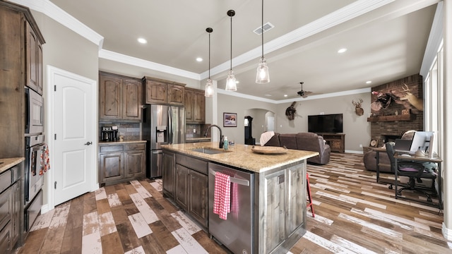 kitchen with ceiling fan, sink, a kitchen island with sink, appliances with stainless steel finishes, and dark wood-type flooring