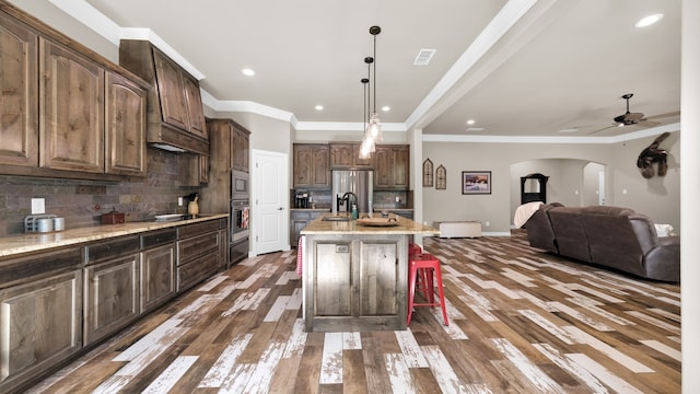 kitchen featuring ceiling fan, backsplash, a center island with sink, and dark wood-type flooring