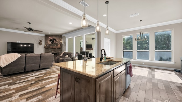 kitchen with ceiling fan with notable chandelier, a kitchen island with sink, brick wall, a stone fireplace, and sink