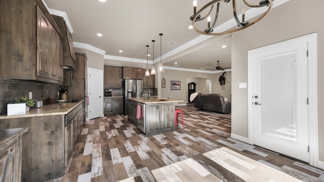 kitchen with backsplash, ceiling fan with notable chandelier, dark hardwood / wood-style flooring, pendant lighting, and a center island with sink