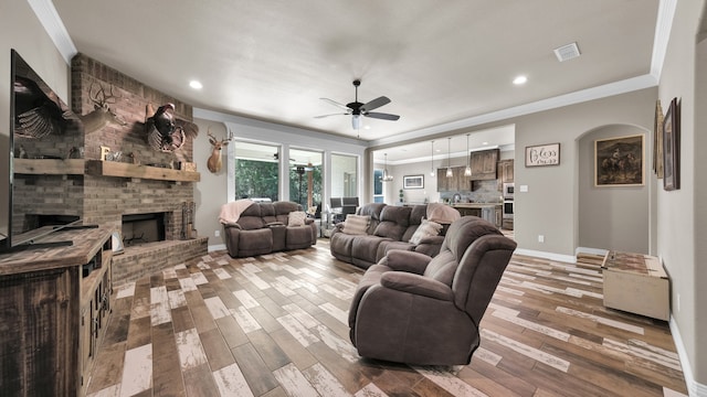 living room featuring ornamental molding, wood-type flooring, a brick fireplace, and ceiling fan