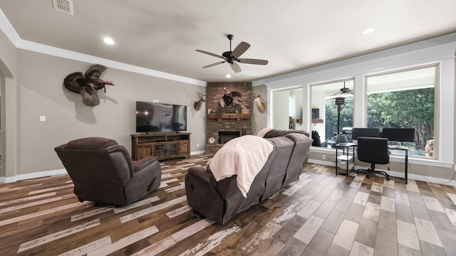 living room with ceiling fan, a brick fireplace, brick wall, hardwood / wood-style floors, and ornamental molding