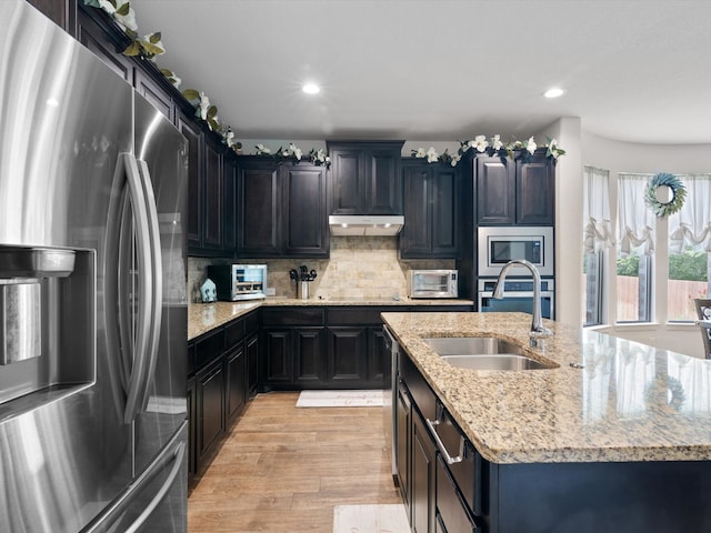 kitchen featuring decorative backsplash, light hardwood / wood-style flooring, sink, light stone countertops, and appliances with stainless steel finishes