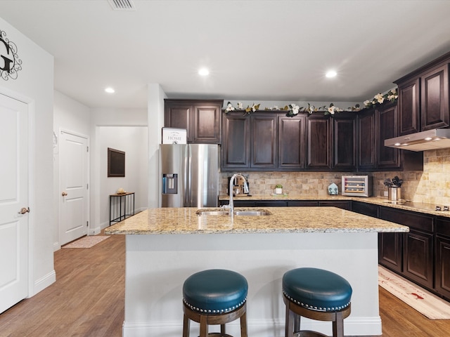 kitchen with dark brown cabinets, an island with sink, stainless steel refrigerator with ice dispenser, and wood-type flooring