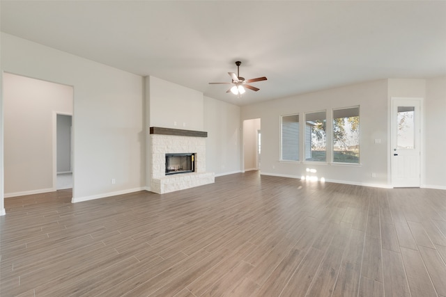 unfurnished living room featuring ceiling fan, a stone fireplace, and light wood-type flooring