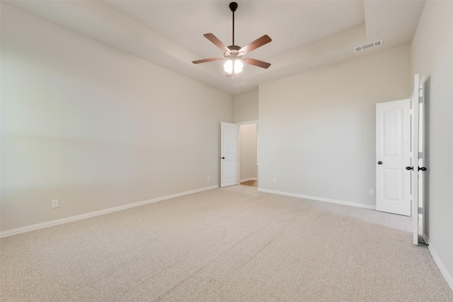 spare room featuring a high ceiling, light carpet, ceiling fan, and a tray ceiling