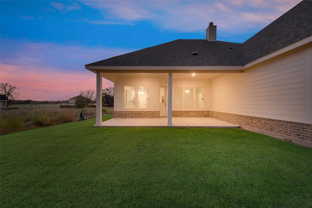 back house at dusk with a lawn and a patio area