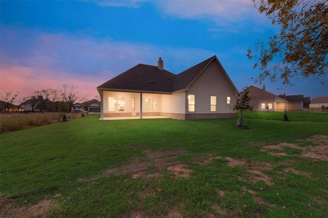 back house at dusk featuring a patio and a yard