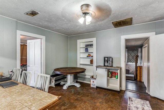 dining area featuring ceiling fan, wooden walls, and a textured ceiling