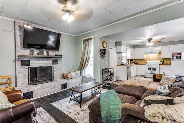 living room with crown molding, ceiling fan, a brick fireplace, and light wood-type flooring