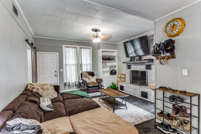 living room featuring crown molding, a brick fireplace, ceiling fan, a barn door, and hardwood / wood-style floors