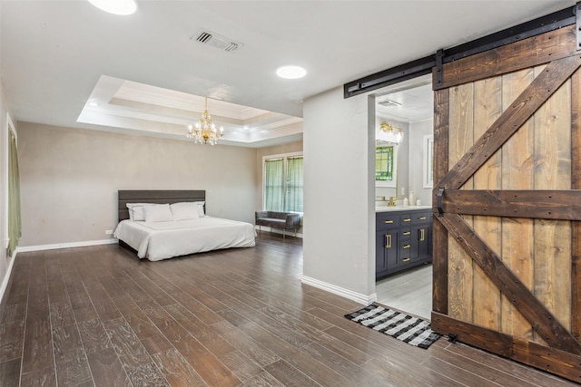 unfurnished bedroom with a barn door, hardwood / wood-style flooring, a raised ceiling, ensuite bath, and a chandelier