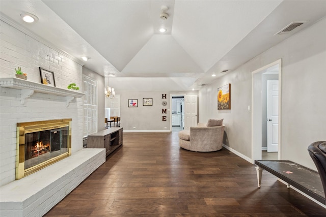 living room with lofted ceiling, a brick fireplace, dark hardwood / wood-style flooring, and a chandelier