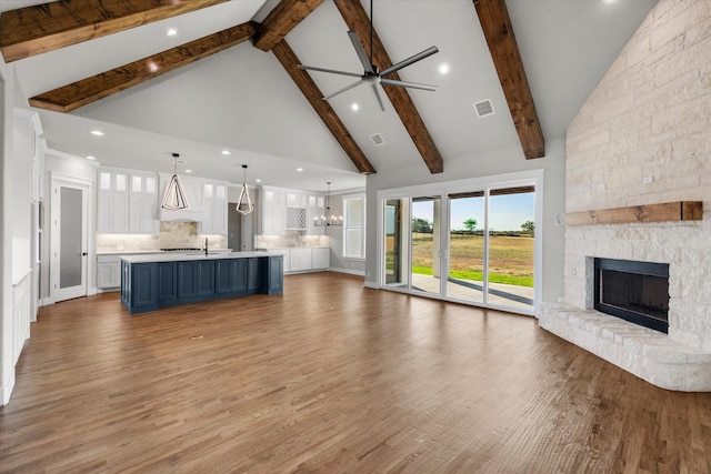 unfurnished living room with high vaulted ceiling, light wood-type flooring, beamed ceiling, and a stone fireplace