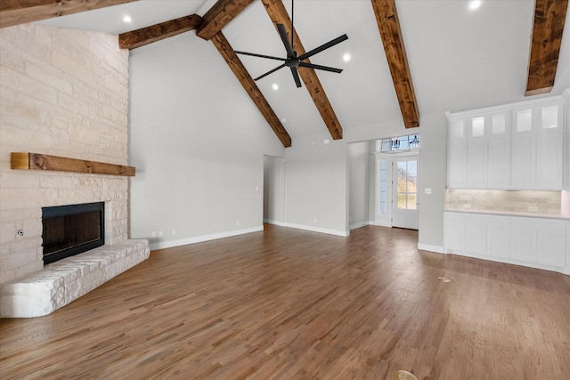 unfurnished living room with beamed ceiling, high vaulted ceiling, wood-type flooring, ceiling fan, and a stone fireplace