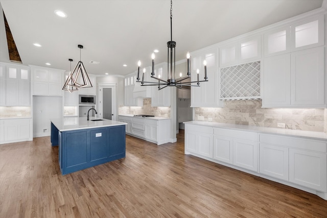 kitchen with light hardwood / wood-style flooring, backsplash, pendant lighting, white cabinets, and a center island with sink