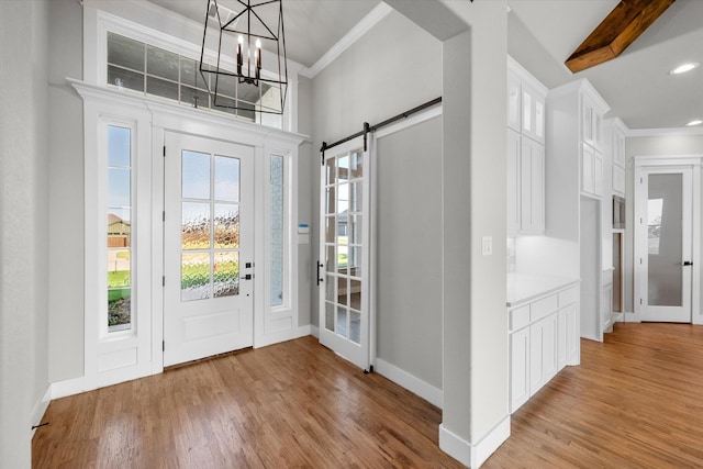 entrance foyer featuring a barn door, a high ceiling, beam ceiling, light hardwood / wood-style floors, and a notable chandelier