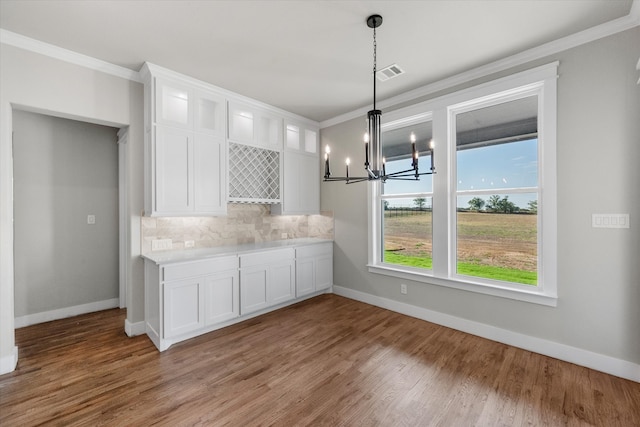 kitchen featuring tasteful backsplash, hardwood / wood-style floors, ornamental molding, white cabinets, and an inviting chandelier