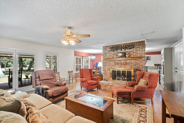 living room featuring light hardwood / wood-style floors, a textured ceiling, a brick fireplace, and ceiling fan with notable chandelier