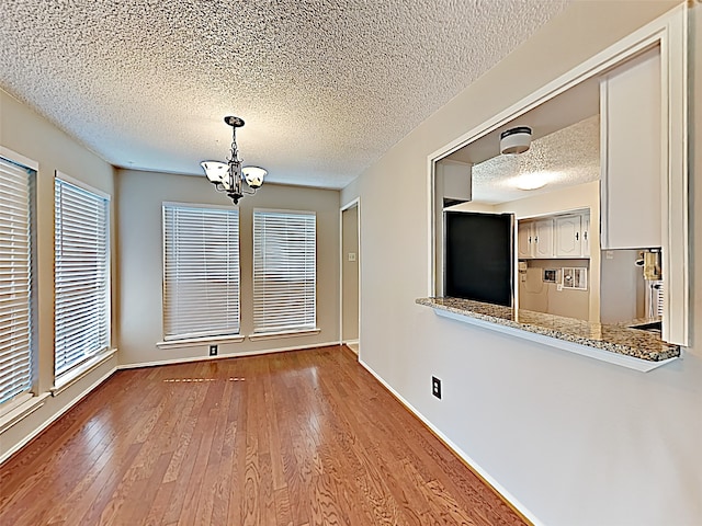 unfurnished dining area featuring plenty of natural light, a notable chandelier, hardwood / wood-style floors, and a textured ceiling