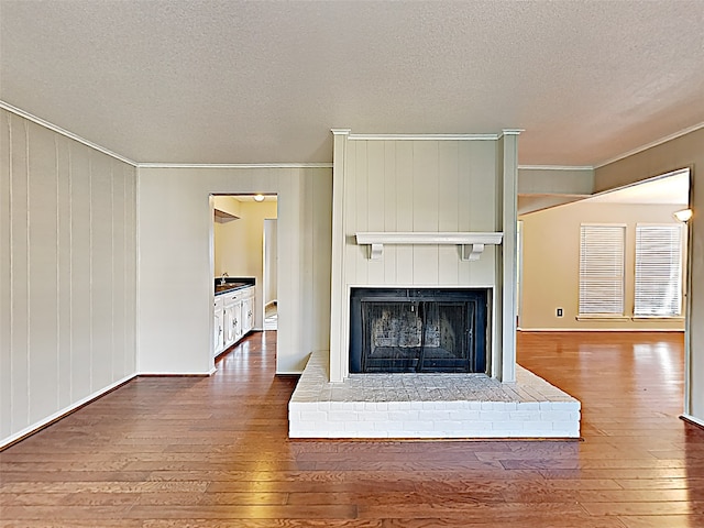 unfurnished living room featuring sink, a fireplace, a textured ceiling, dark wood-type flooring, and ornamental molding