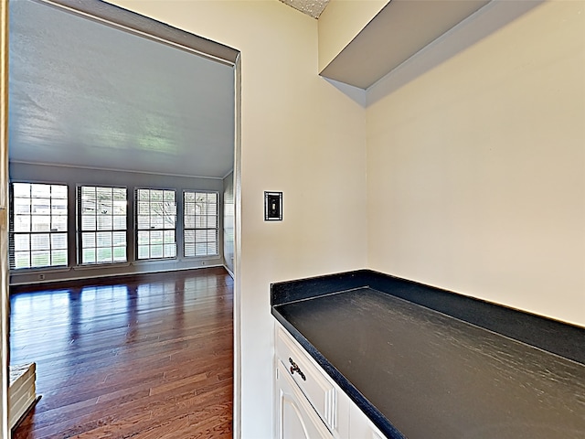 interior space with dark countertops, open floor plan, white cabinets, a textured ceiling, and wood finished floors