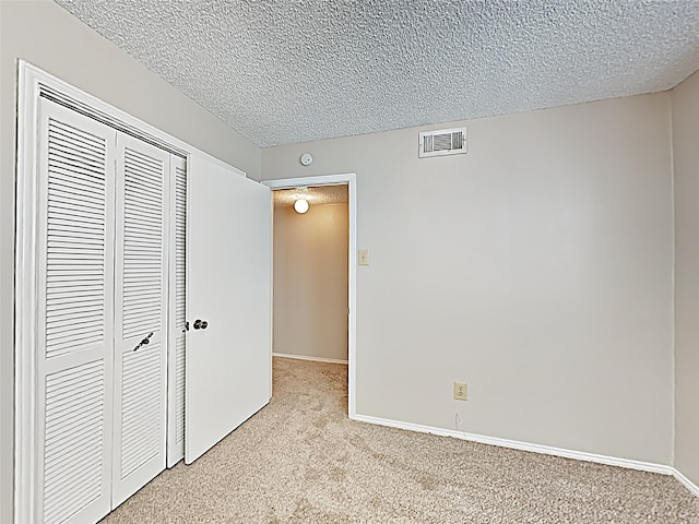 unfurnished bedroom with a closet, light colored carpet, visible vents, a textured ceiling, and baseboards