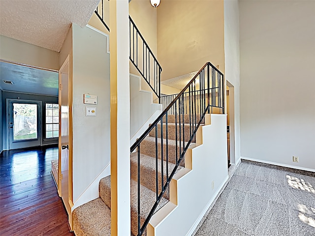 stairway with a high ceiling, a textured ceiling, baseboards, and wood finished floors