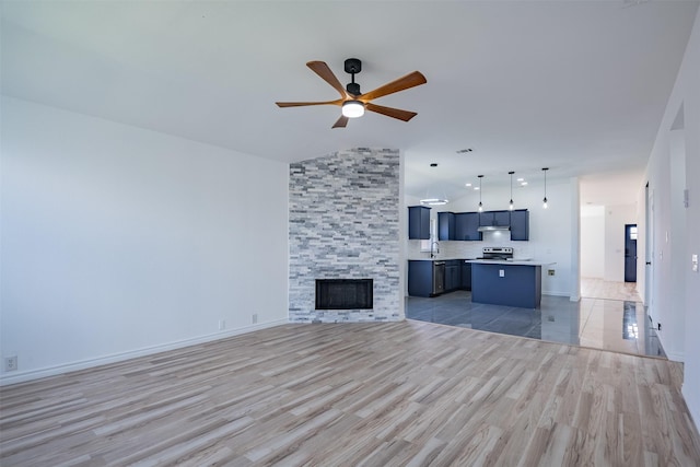 unfurnished living room with lofted ceiling, wood-type flooring, sink, ceiling fan, and a tile fireplace