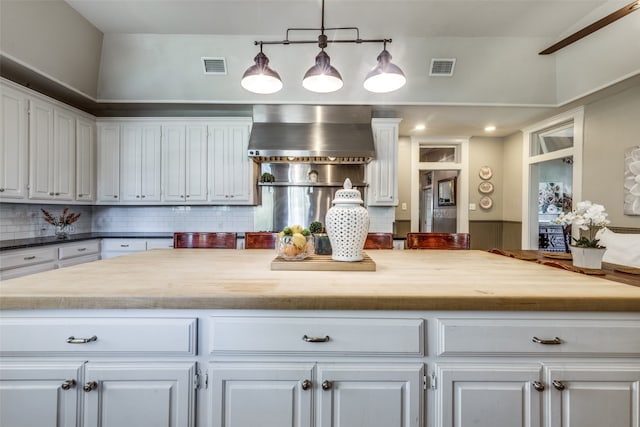 kitchen featuring tasteful backsplash, wall chimney exhaust hood, white cabinetry, and wooden counters