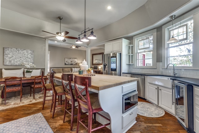 kitchen with hanging light fixtures, appliances with stainless steel finishes, white cabinetry, wooden counters, and ceiling fan