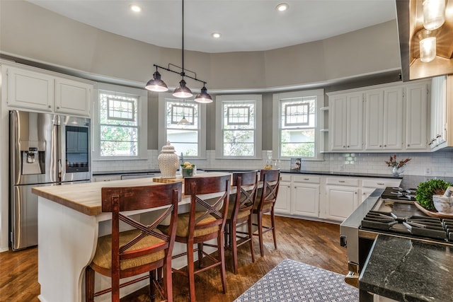 kitchen with a kitchen island, stainless steel fridge, wood counters, a kitchen bar, and plenty of natural light