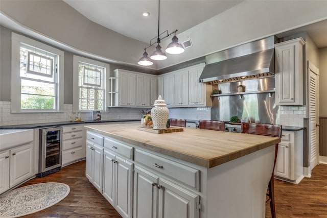 kitchen featuring wall chimney range hood, a kitchen island, white cabinetry, and beverage cooler